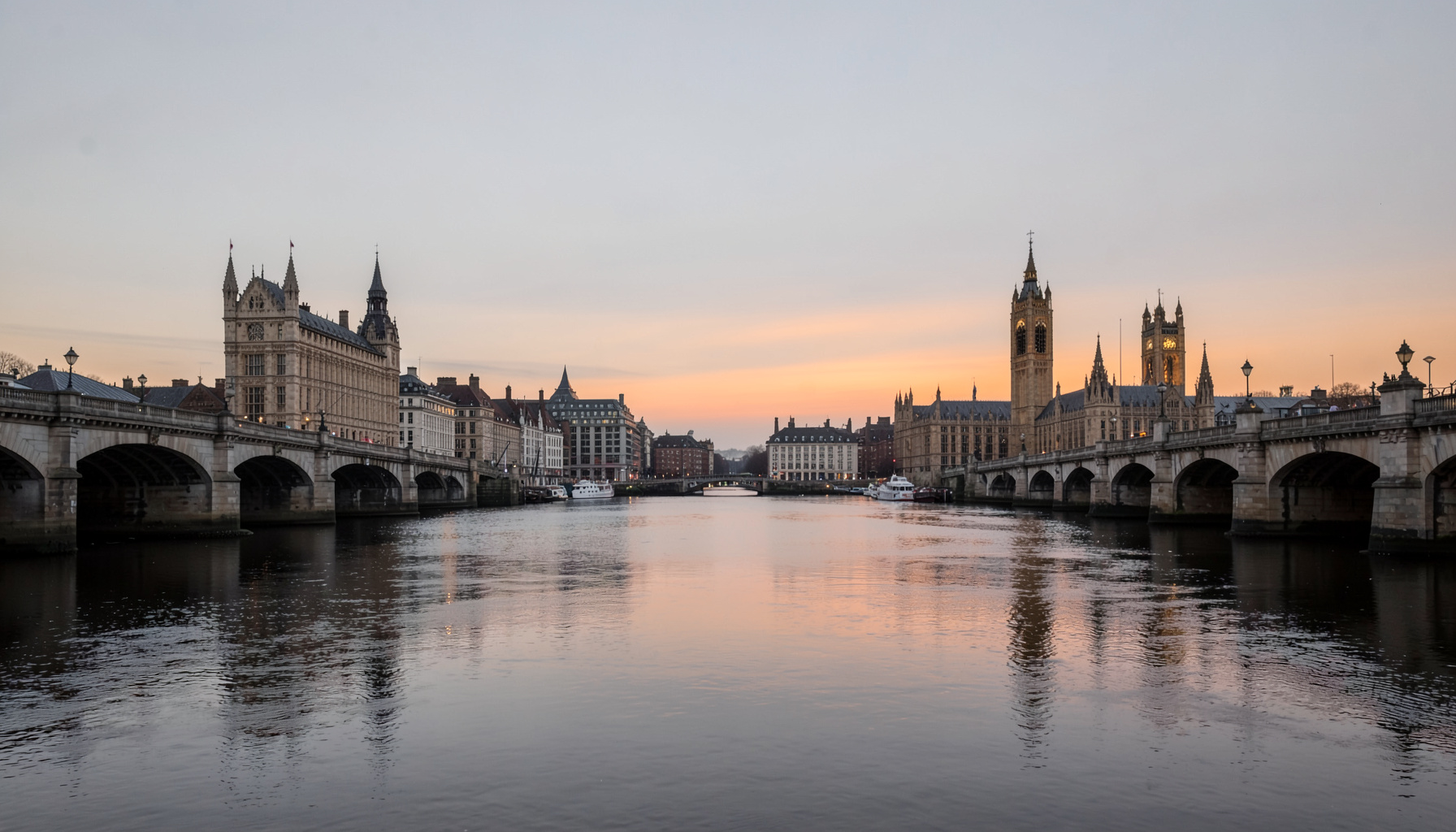 A clean architectural photograph of London's skyline at dusk, with the River Thames reflecting soft grey and amber light, framed by symmetrical bridge lines and muted stone tones.